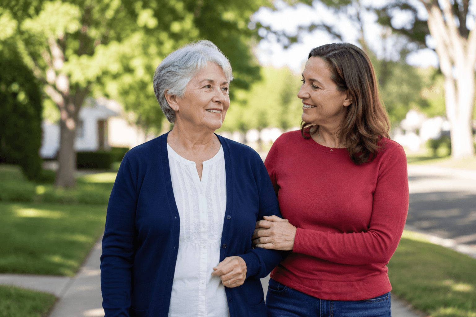 An older woman walking arm in arm with her daughter on a tree-lined sidewalk.